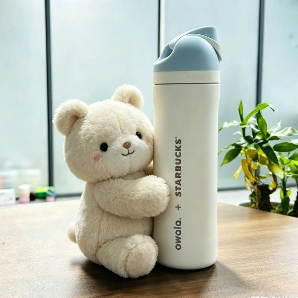 A fluffy cream-colored teddy bear sits next to a white Owala insulated tumbler with a light blue lid.