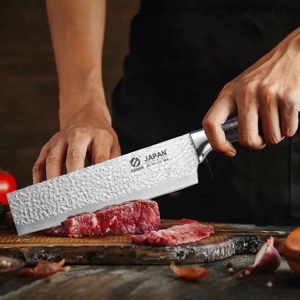 Eine Hand hält ein japanisches Edelstahlkochmesser, das rotes Fleisch auf einem Holzbrett schneidet.