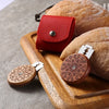 A red leather bread scoring tool rests on a wooden board next to a loaf of bread.