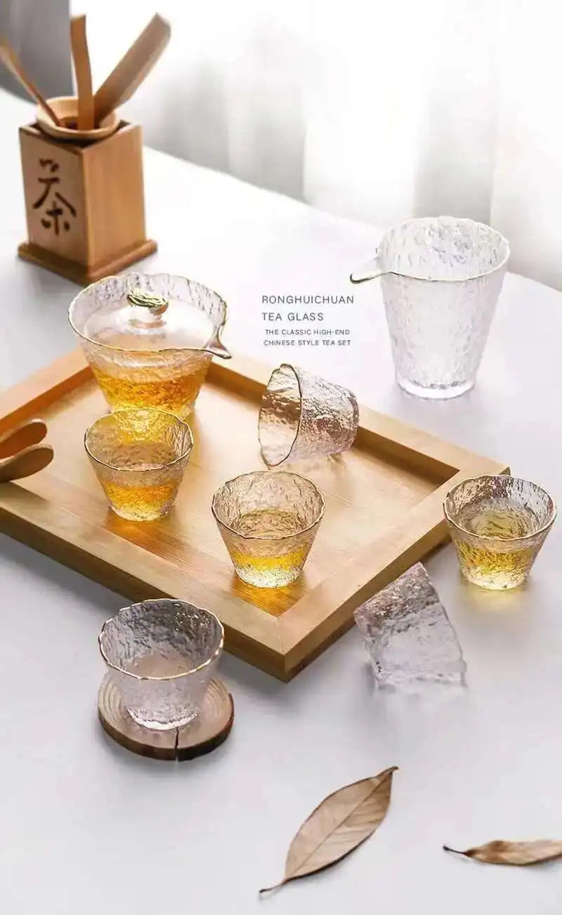 A set of elegant glass tea cups and accessories for a Chinese or Japanese ceremony displayed on a wooden tray.