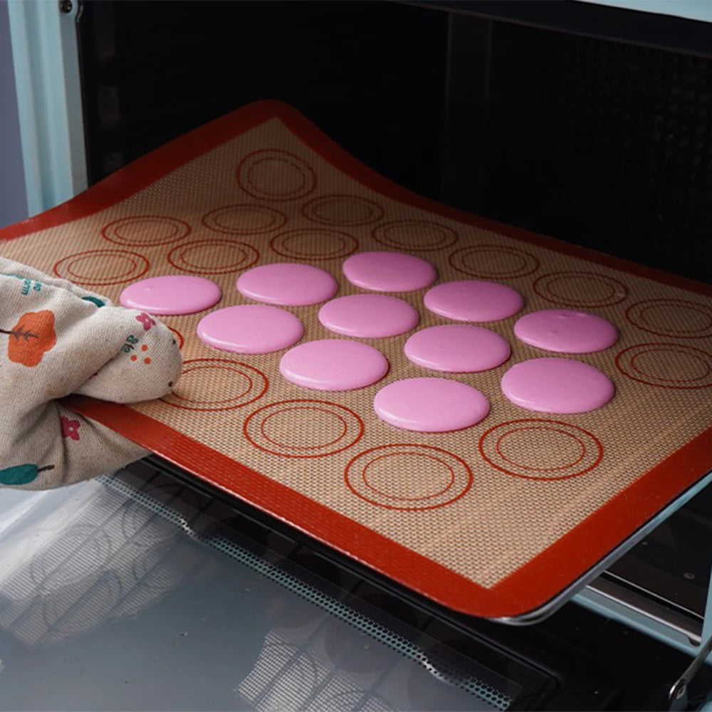 A silicone baking mat liner with pink and orange circular indentations is placed on a dark oven rack.