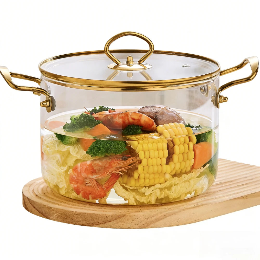 A clear glass cookware pot with a lid and double handles filled with cooked shrimp, corn, and vegetables on a wooden board.