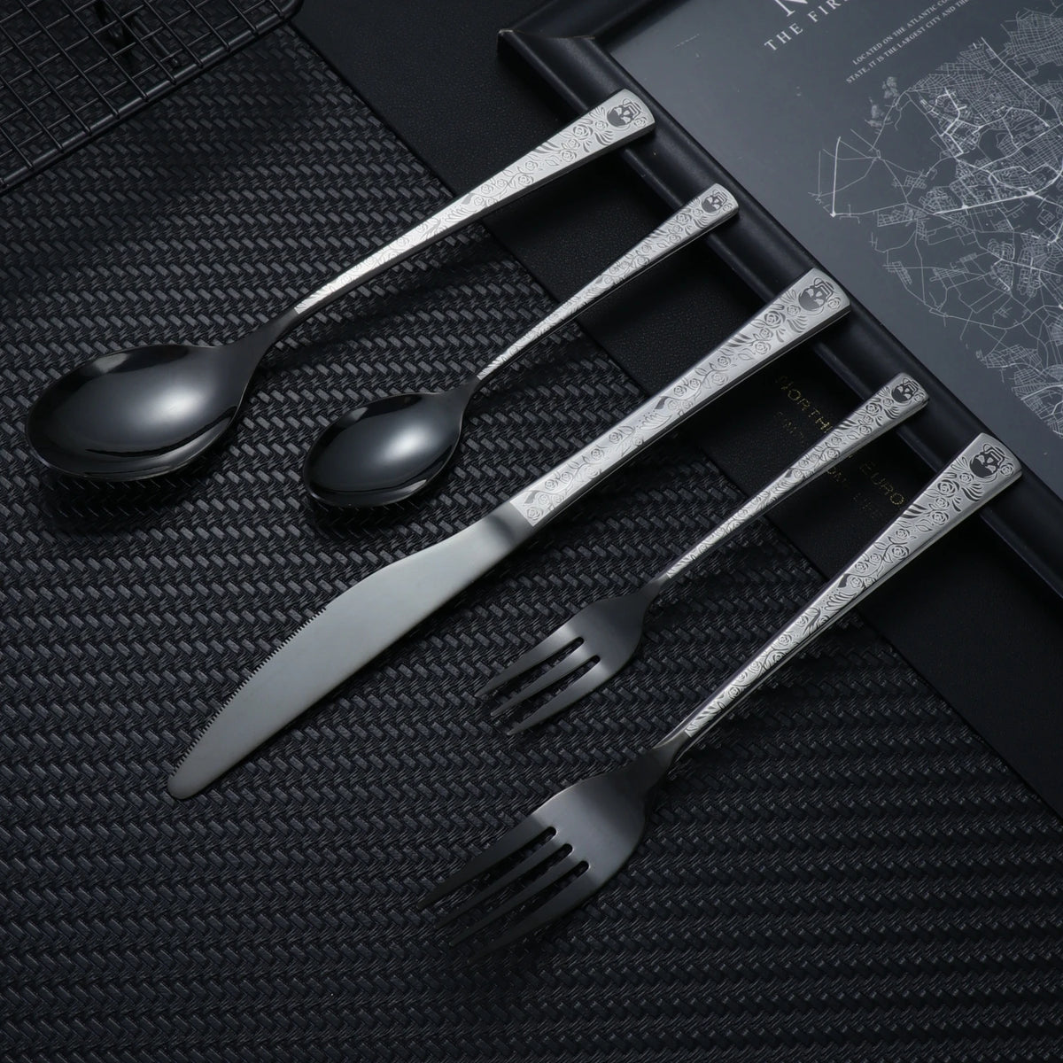 A set of stainless steel cutlery, including a spoon, knife, and fork, featuring a skull pattern design.
