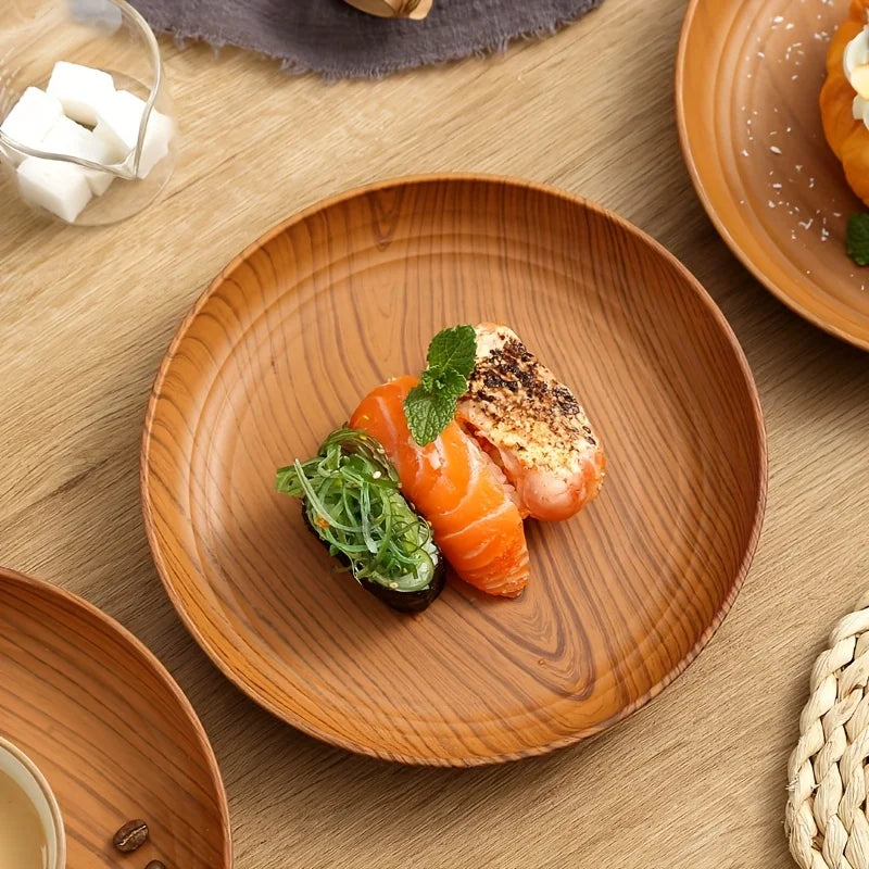 A wooden plate features smoked salmon and greens, served alongside a small glass of white cubes.