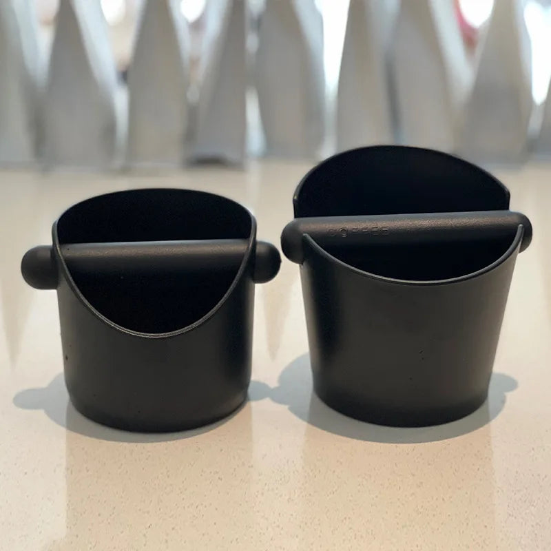 A black espresso knock box with a hinged lid is shown on a white surface.