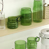 A set of elegant green glass teacups and mugs displayed on a light wooden shelf.