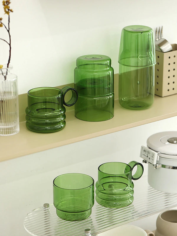 A set of elegant green glass teacups and mugs displayed on a light wooden shelf.
