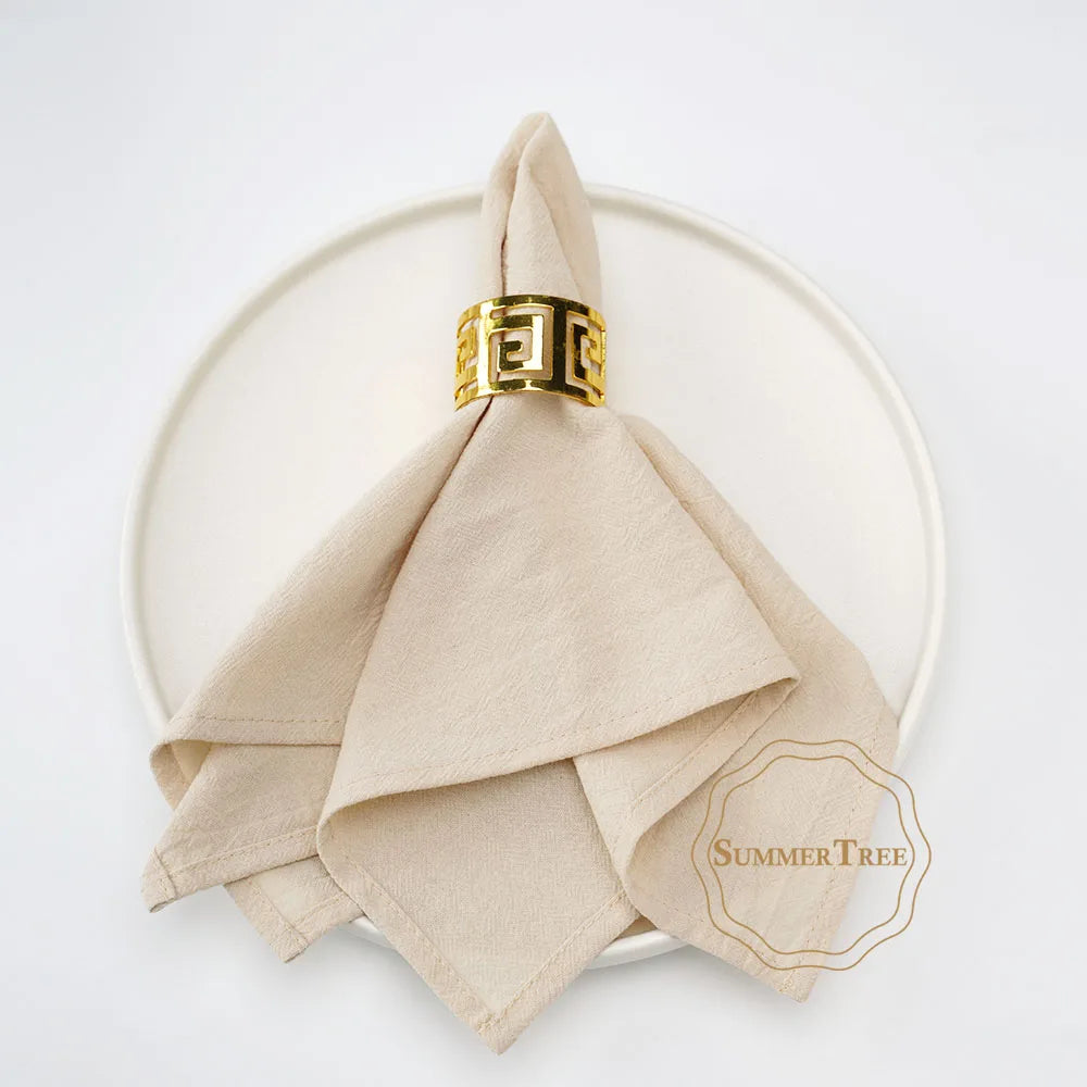 A stack of ten beige cotton table napkins tied with a gold patterned ribbon placed on a white plate.