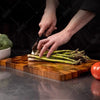 A hand is cutting asparagus on a wooden cutting board.
