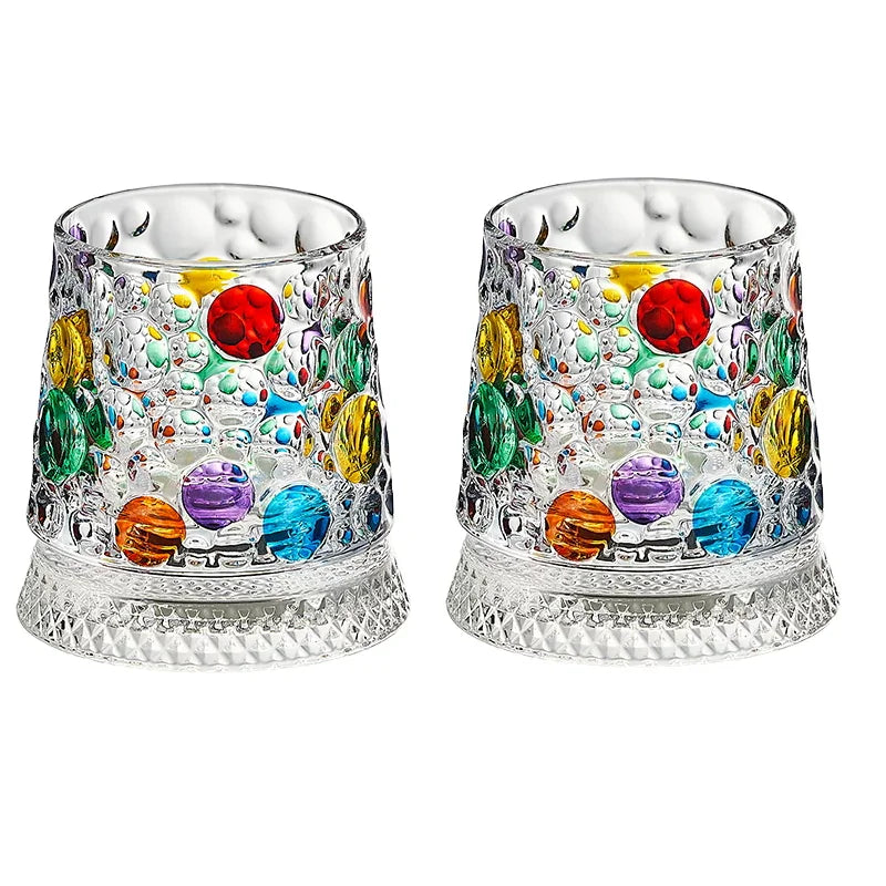 A pair of textured, faceted rotating whiskey glasses filled with colorful glass beads and stones.