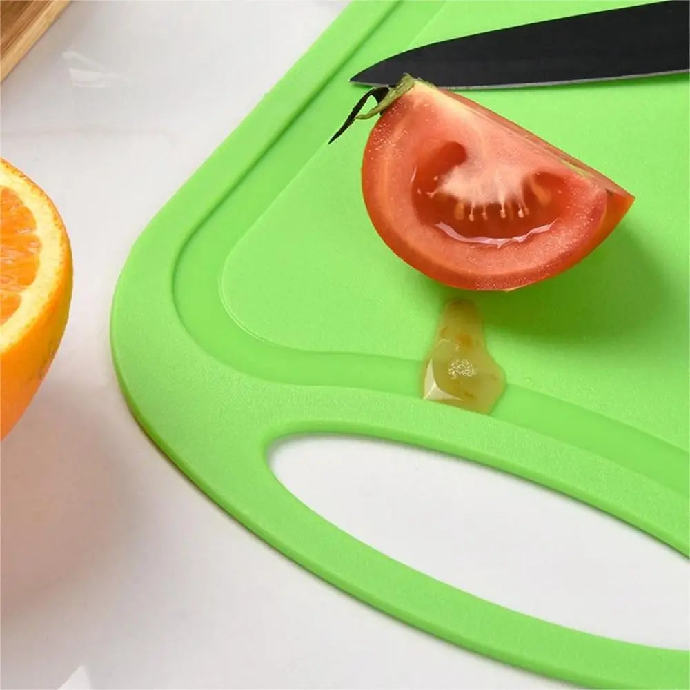 A green non-slip plastic cutting board features a tomato slice and a small piece of fruit on its surface.