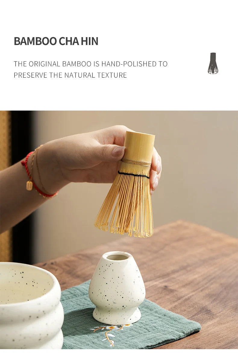 A hand holds a bamboo chashitsu whisk used for preparing matcha tea, next to a ceramic bowl.