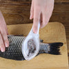 A hand is using a clear tool to scrape or grate the scales off a fish skin on a wooden board.