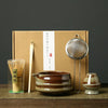 A set of Japanese matcha whisks and a ceramic bowl are displayed in a cardboard box.