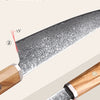 Close-up view of a Damascus steel kitchen knife showing an arc-curve design and a 15 degree golden V-shaped edge.