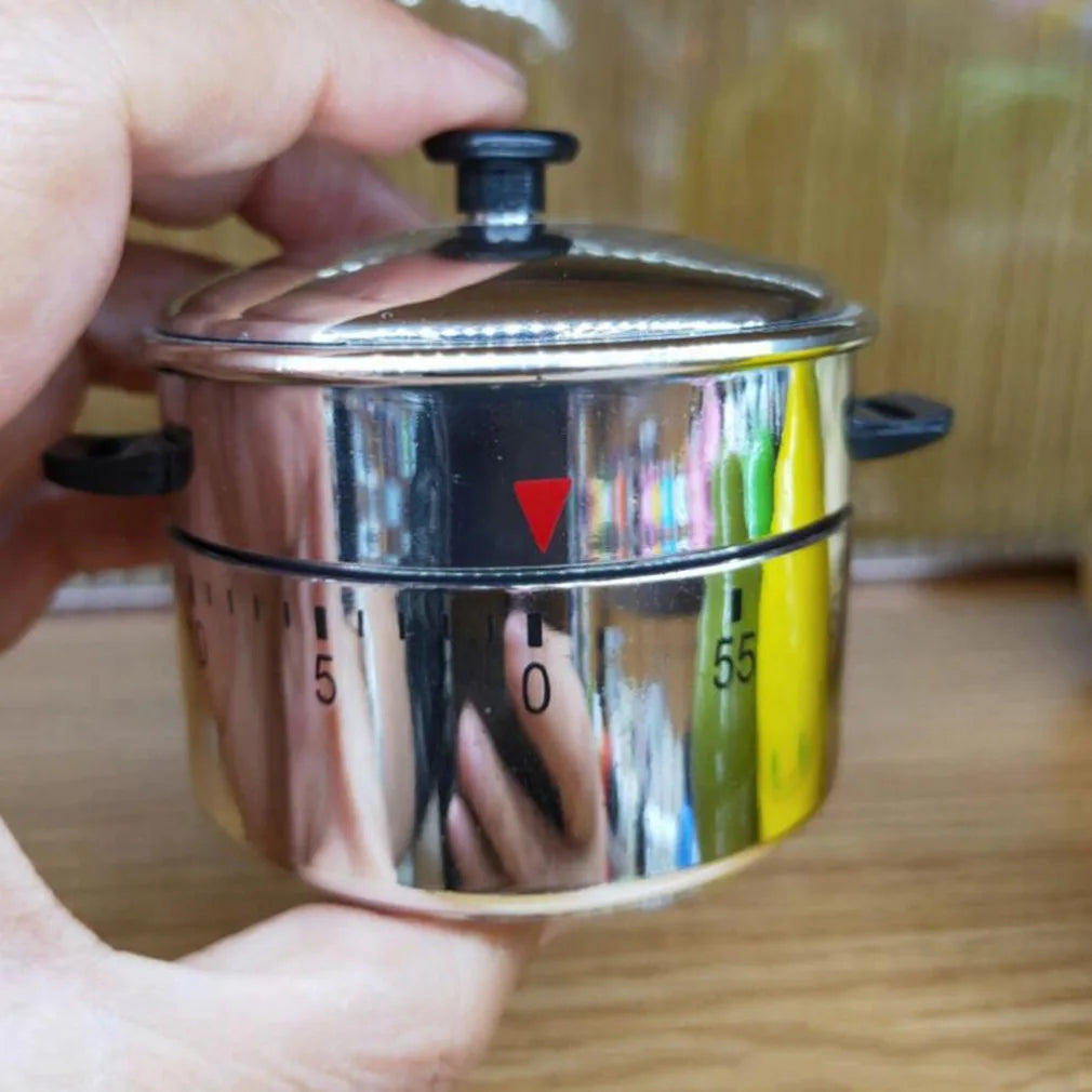 A hand holds a stainless steel mechanical kitchen cooking timer with markings and a lid.