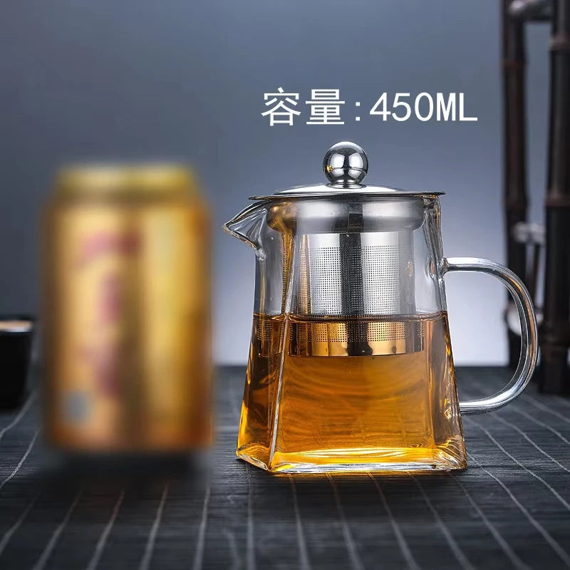 A clear glass teapot filled with amber liquid, featuring a stainless steel infuser, set on a dark surface.