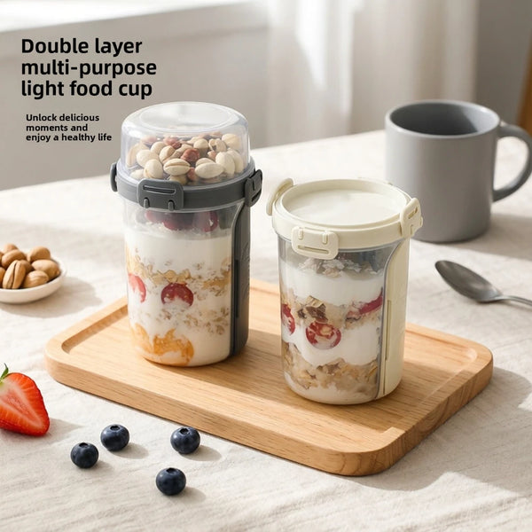 A double-layer container of overnight oats with a clear lid sits on a wooden board next to a mug and fresh berries.
