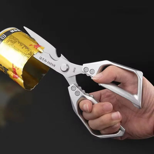 Eine Hand hält eine Edelstahl-Küchenschere mit einer gelben Dose im Hintergrund sichtbar.