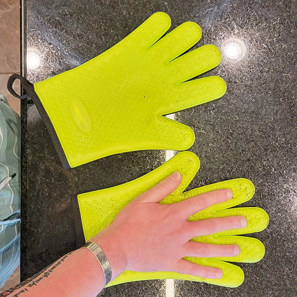A hand wearing bright yellow silicone oven gloves is shown resting on a dark countertop.