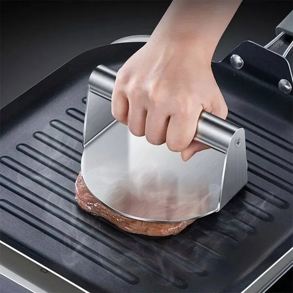 Eine Hand drückt ein rundes Fleischstück auf eine Edelstahlpresse für Burger-Patties auf ein Grillgitter.