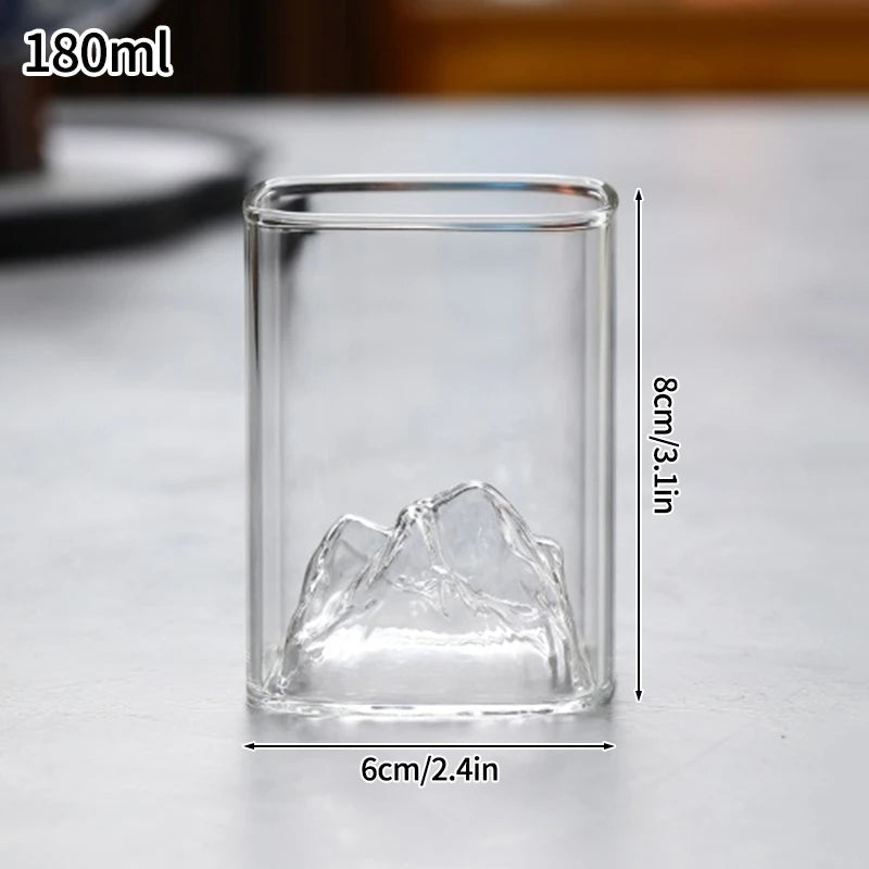 A clear glass tumbler with a jagged ice-like shape is shown on a light surface.