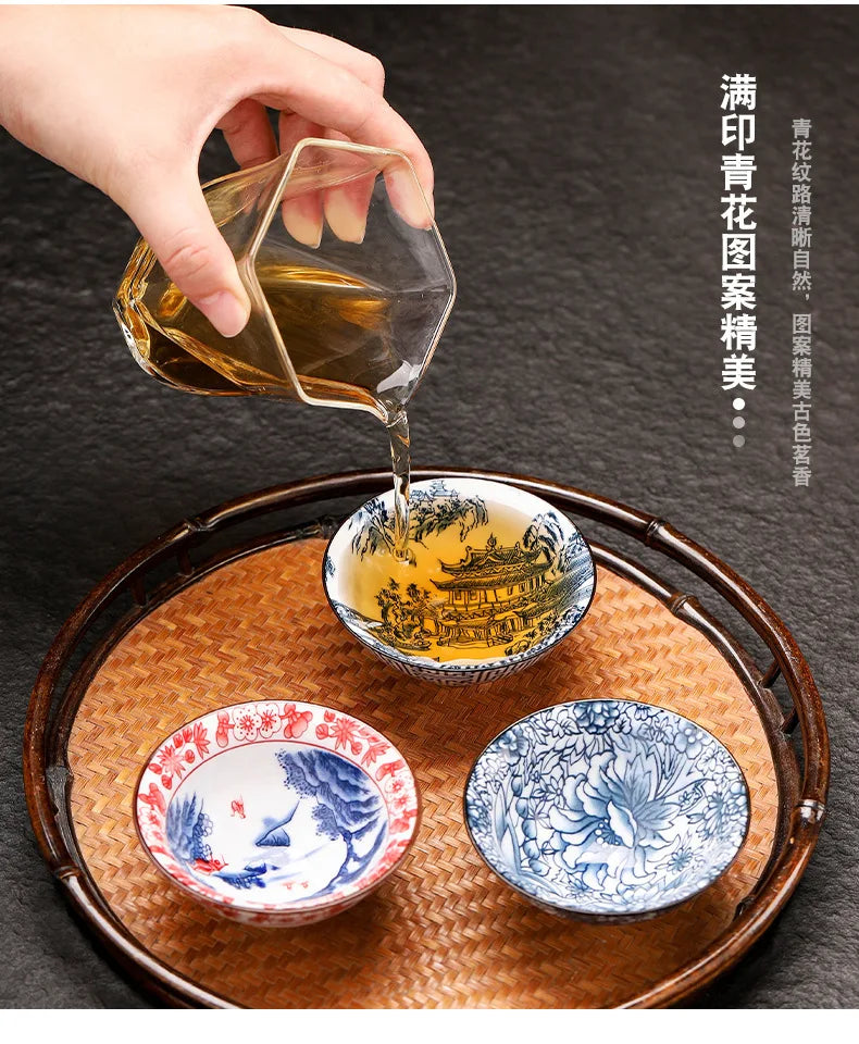 A hand pours amber liquid from a glass into a small bowl, with blue and white porcelain dishes arranged on a woven tray.