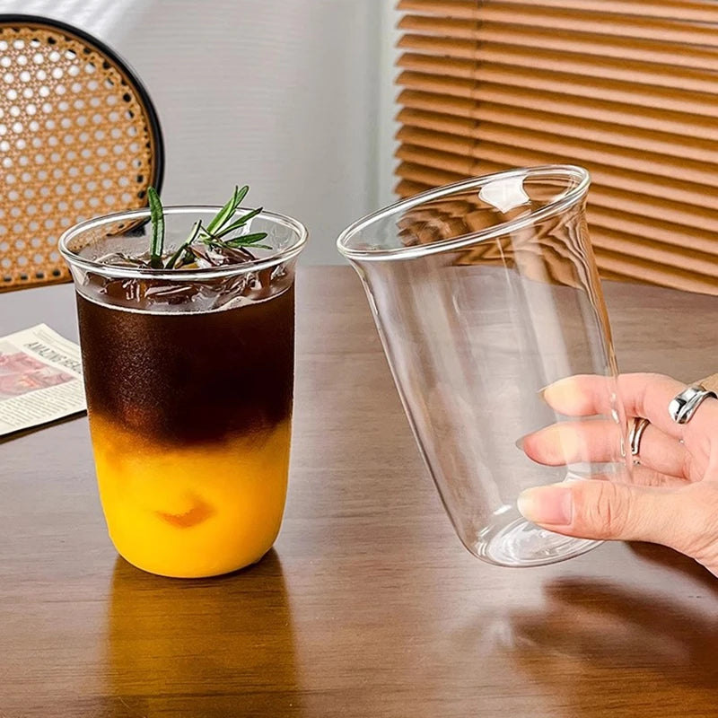 A clear glass tumbler filled with iced tea, resting on a wooden table.