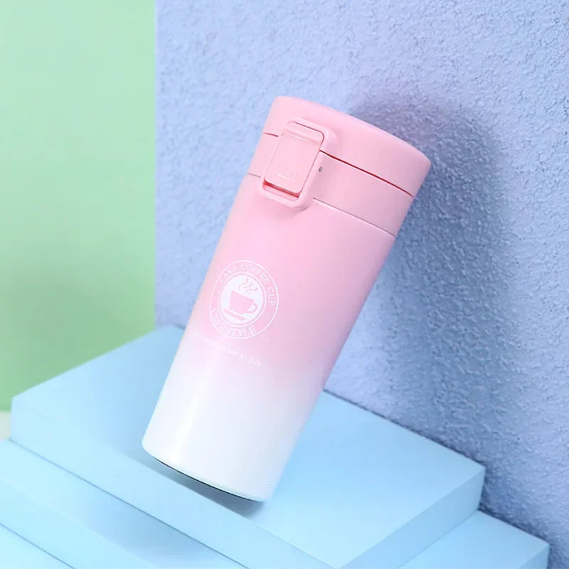 A pink double-walled stainless steel thermal travel mug resting on a light blue surface against a gray wall.