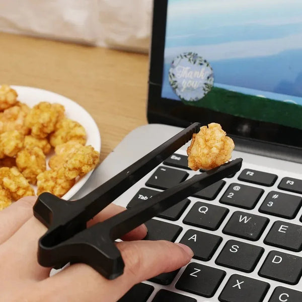 Eine Hand hält schwarze Finger-Stäbchen-Stäbchen auf einer Laptop-Tastatur neben goldenen Snacks.