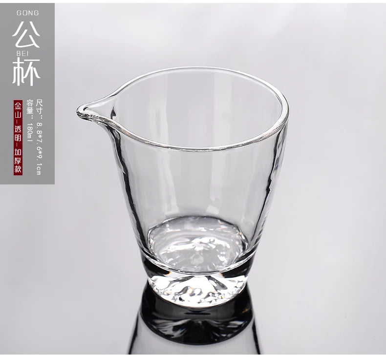 A clear glass teapot or pourer is shown, filled with a light liquid, set against a white background.