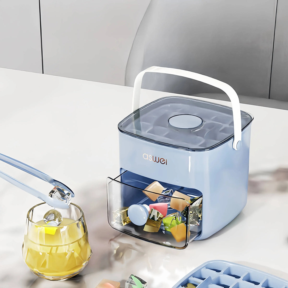 A light blue ice cube maker with a clear lid and double layer design sits on a white surface next to a glass of juice.