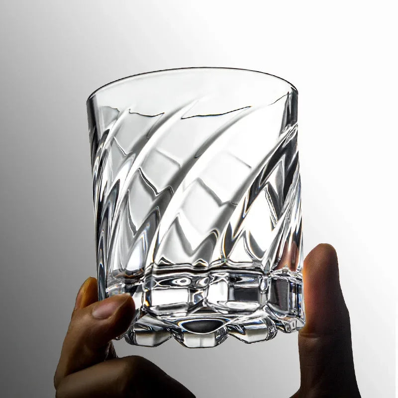 Una mano sostiene un vaso de whisky claro y texturizado para cócteles contra un fondo gris claro.