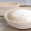 A white natural rattan bread proofing basket filled with white flour sits on a wooden surface.