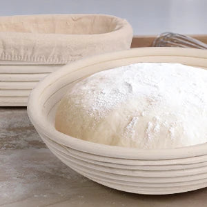 A white natural rattan bread proofing basket filled with white flour sits on a wooden surface.