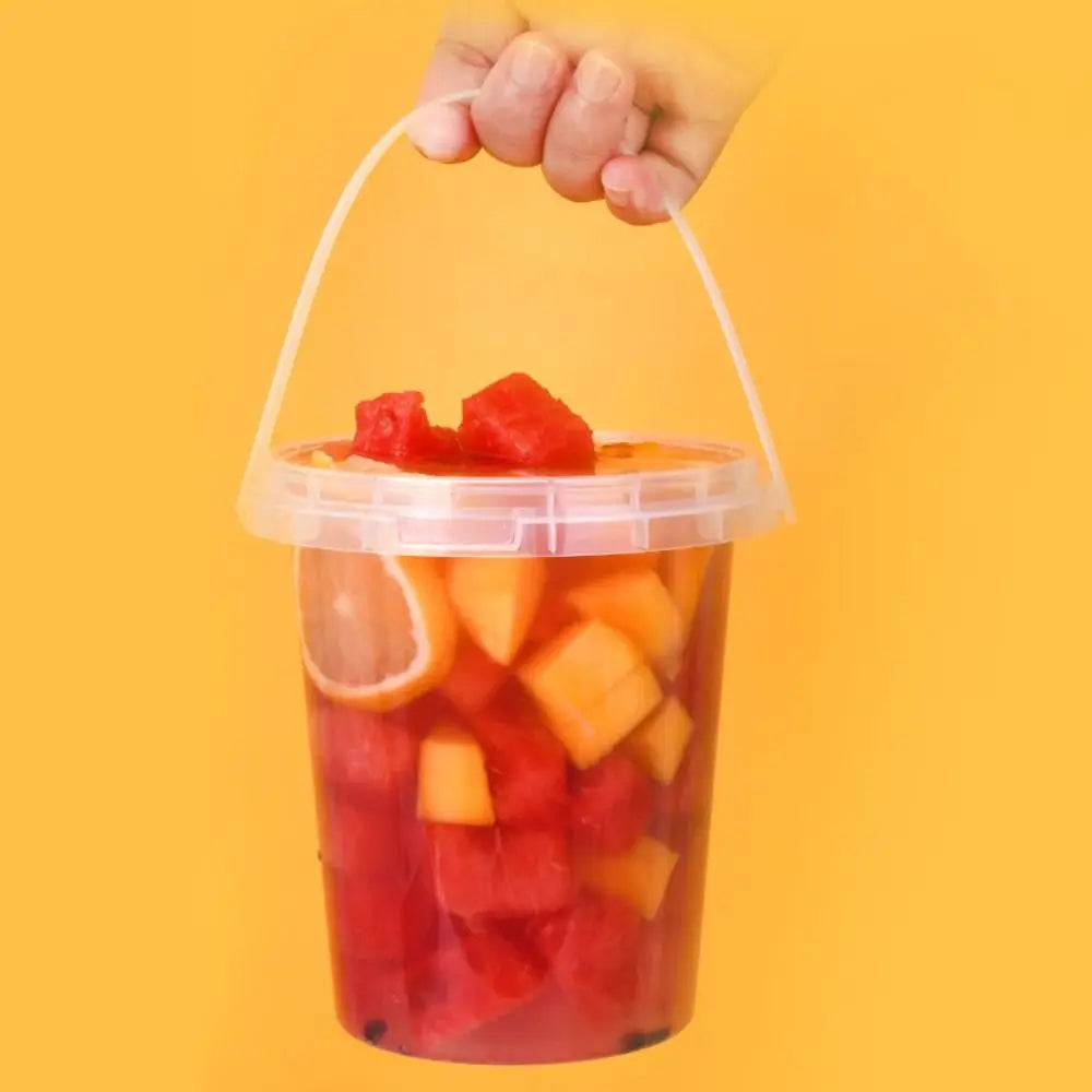 A hand is holding a clear plastic storage bucket filled with diced watermelon and citrus fruit.