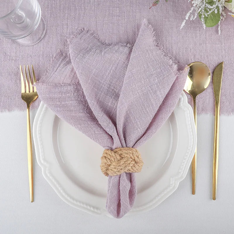 Un juego de servilletas de gasa de lavanda reutilizables atadas con cuerda de yute sobre un plato y cubiertos blancos.