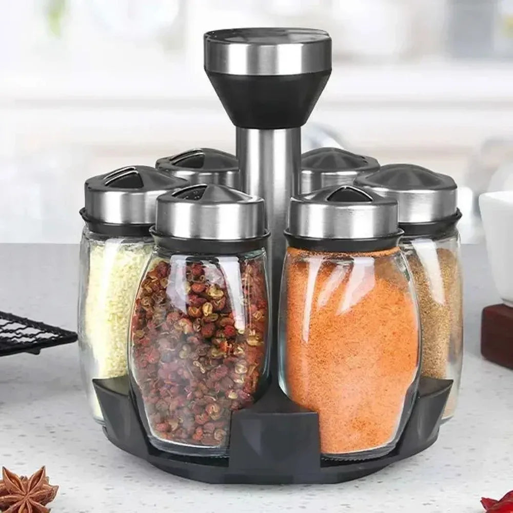 A set of rotating glass spice jars with silver lids and black bases for kitchen organization.