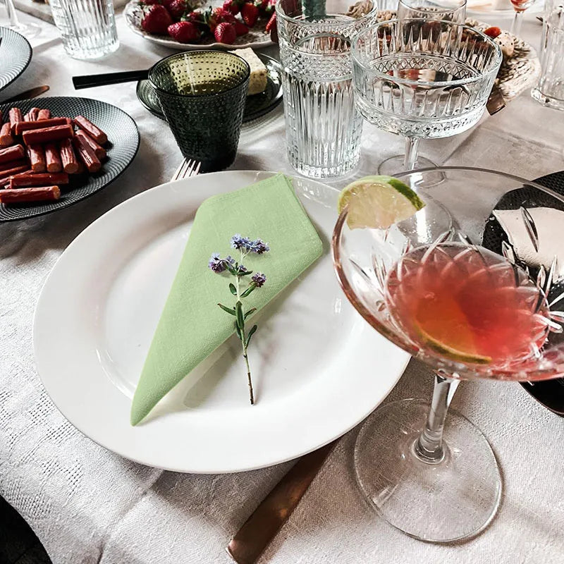 A set of six burgundy cloth napkins is displayed on a white plate amidst glassware and dining setting.