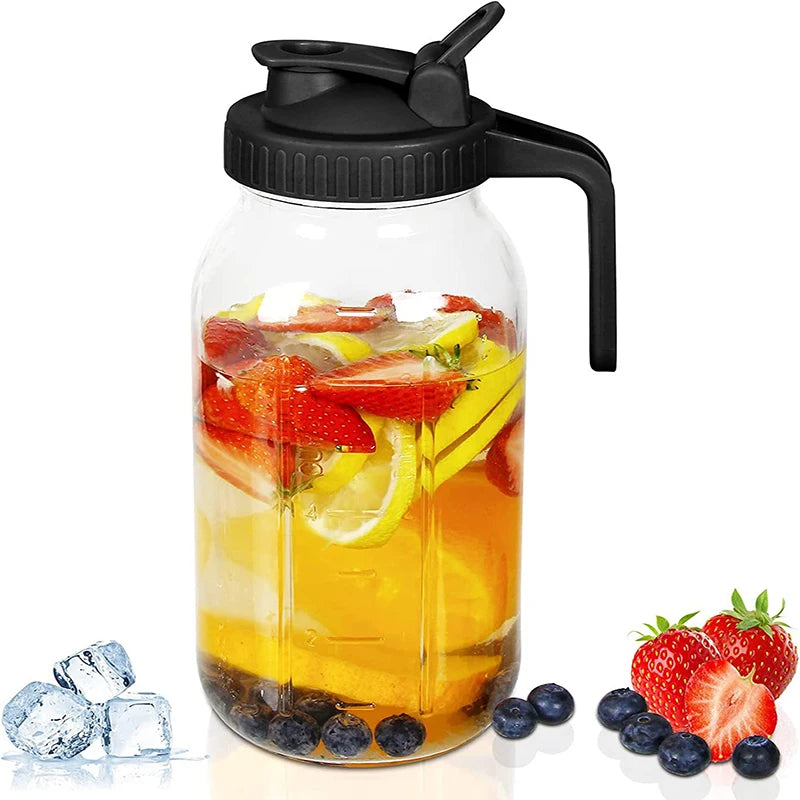 Botella de vidrio transparente llena de jugo de naranja y fruta cortada, con asa negra.
