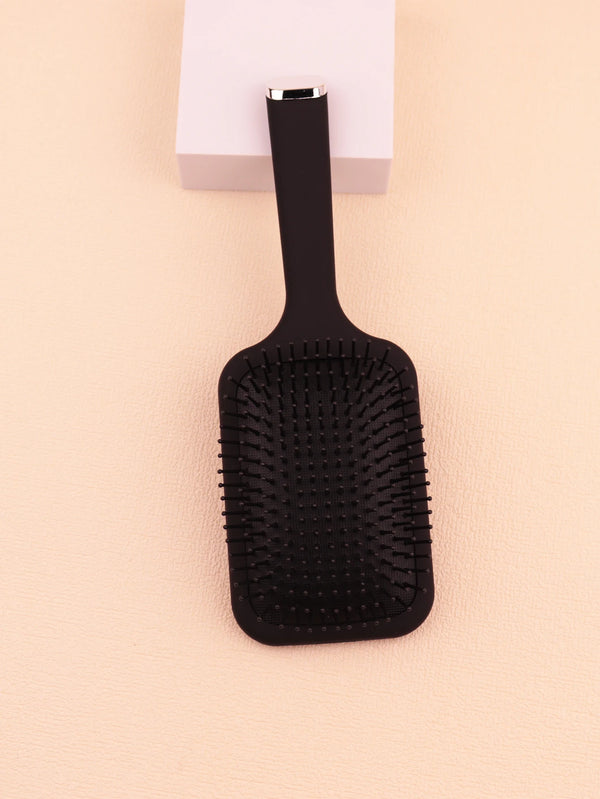 A black anti-static plastic scalp massage comb with a silver handle resting on a light background.