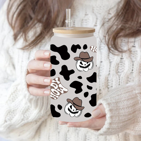 A hand holds a clear tumbler with a black and white leopard print sticker featuring a skull and a hat.