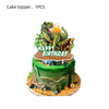 A cake topper featuring a green dinosaur with an open mouth and a golden sun, set on a green cake decorated with foliage.
