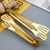 A pair of gold-colored stainless steel BBQ tongs and grill clamps resting on a yellow surface.
