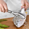 Hands holding a stainless steel fish scale remover tool near a silver fish on a wooden cutting board.