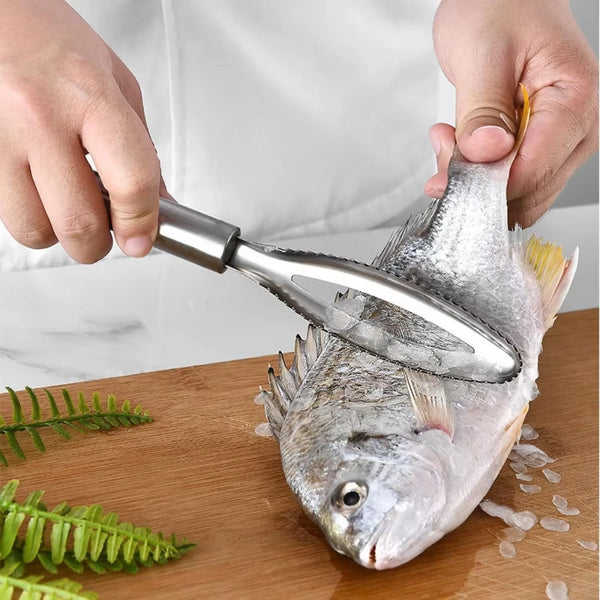 Hände halten ein Edelstahl-Werkzeug zum Entfernen von Fischskalen bei einem silbernen Fisch auf einer Holz-Cutting-Board.
