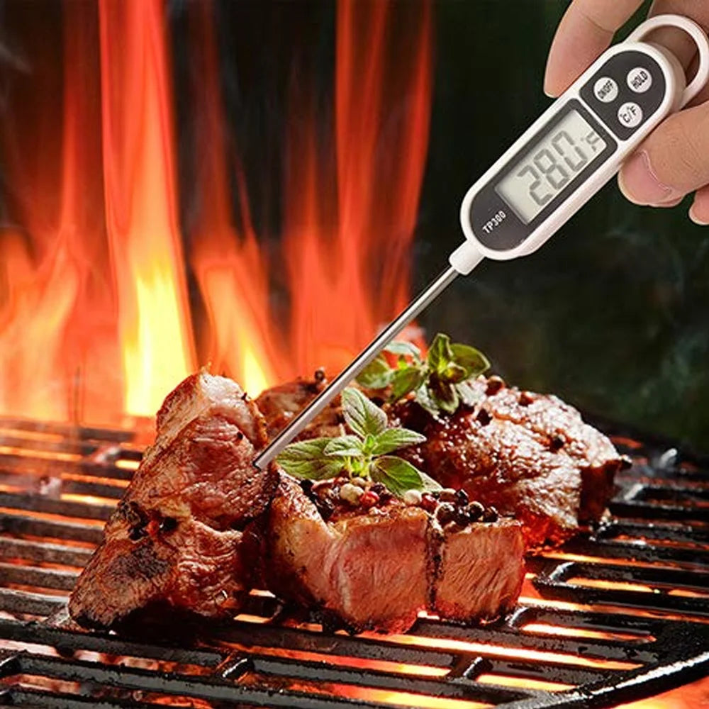 A hand holds a digital meat thermometer with a long probe measuring meat on a grill.