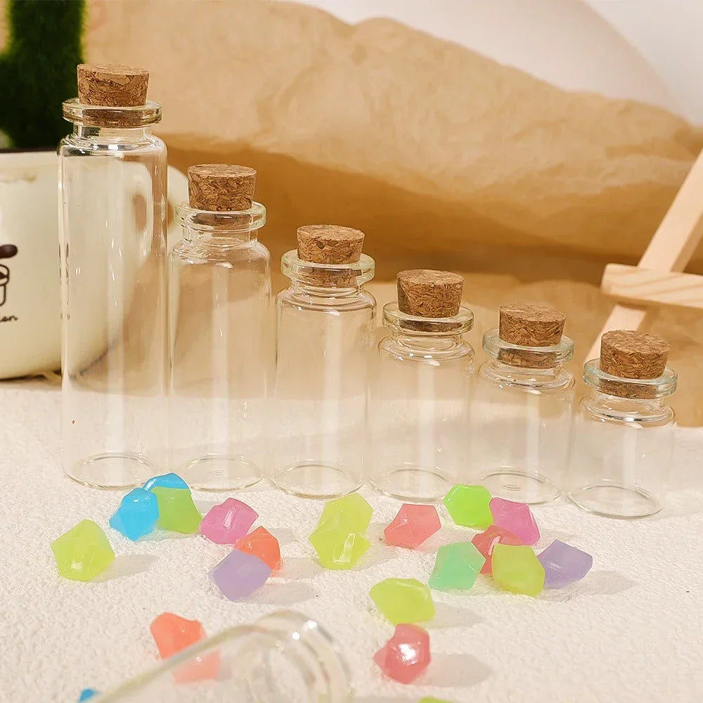 A set of decorative glass bottles filled with colorful glass gems and cork stoppers on a light surface.