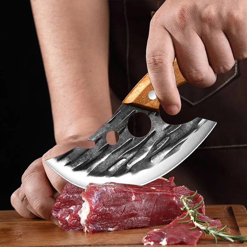 A hand holds a hand forged boning knife slicing raw red meat on a wooden cutting board.