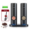 A black electric automatic salt and pepper grinder with a green brush and loose peppercorns visible.